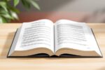Offenes Grundgesetz-Buch auf Schreibtisch mit angedeuteter deutscher Flagge im Hintergrund.