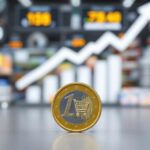 Symbolbild: Eine große Euromünze wird kleiner, im Hintergrund verschwimmen Preise – Darstellung für Inflation.