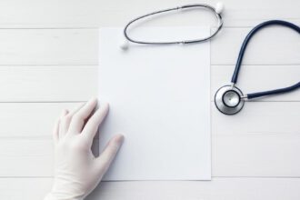 Hand hält Patientenverfügung neben Stethoskop auf Tisch – Symbol für selbstbestimmte medizinische Entscheidungen.