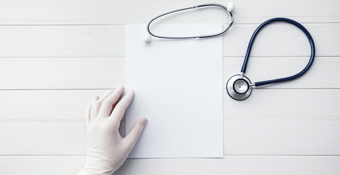 Hand hält Patientenverfügung neben Stethoskop auf Tisch – Symbol für selbstbestimmte medizinische Entscheidungen.