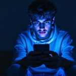 Jugendliche Person blickt besorgt auf ihr Smartphone im abgedunkelten Raum – Symbolbild für Cybermobbing.