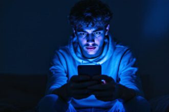 Jugendliche Person blickt besorgt auf ihr Smartphone im abgedunkelten Raum – Symbolbild für Cybermobbing.